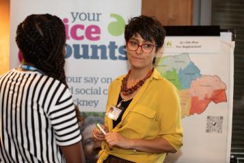 Two women talking in front of a Healthwatch banner