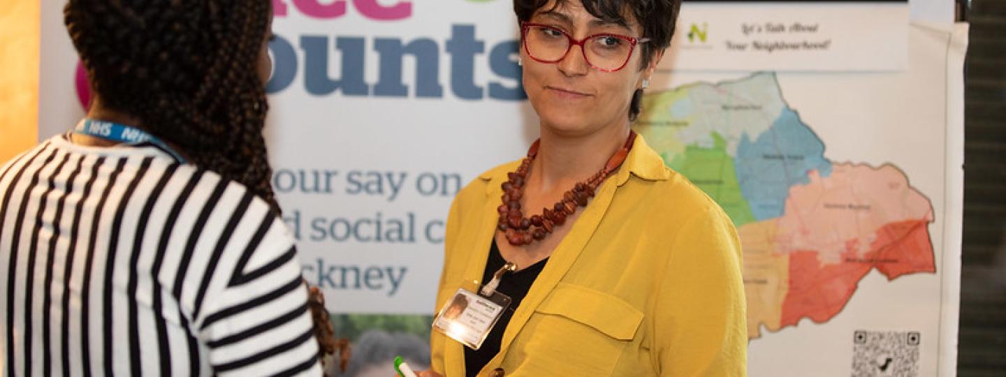 Two women talking in front of a Healthwatch banner